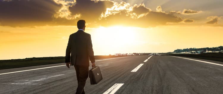 Entrepreneur, carrying a briefcase, walking on an empty highway at sunset.