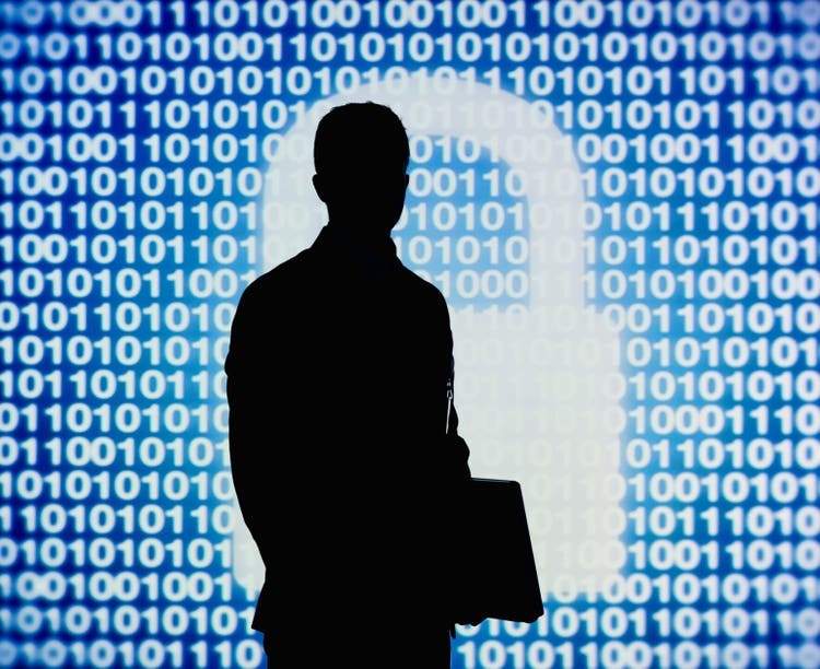 Man standing and holding laptop with code and white figure of a padlock behind him