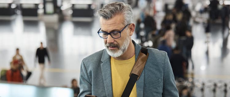 Male commuter using smart phone while standing on escalator. Mature man is holding mobile phone at railroad station. He is wearing blazer.