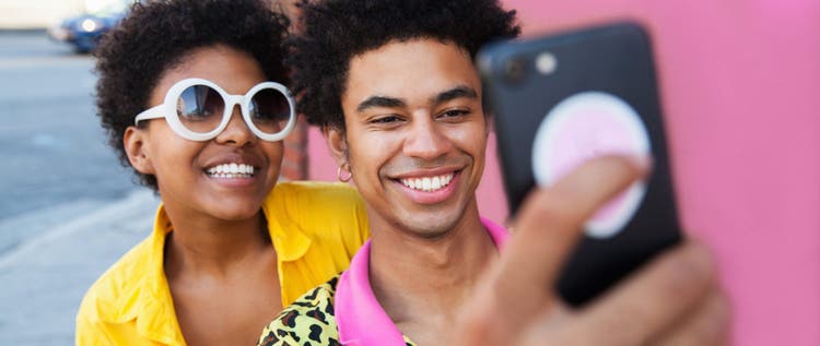 A young couple wearing yellow clothes taking a selfie in front of a pink wall