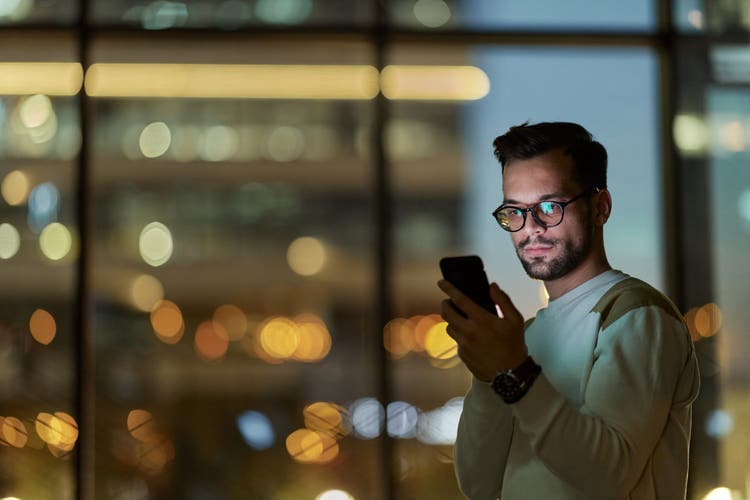 Young man text messaging on cell phone indoors at night.