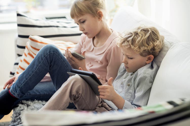 Siblings using technologies on sofa at home