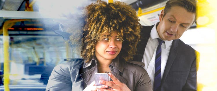 Man looking over a woman's shoulder at her phone on public transit.