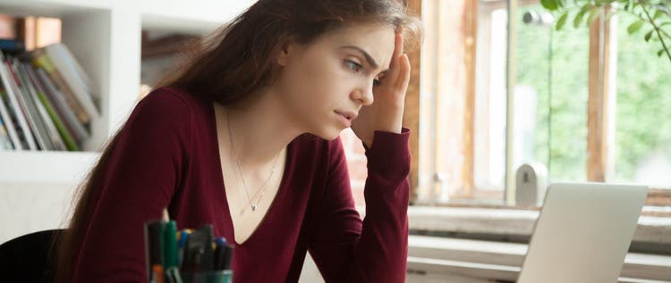 Woman with her hand to her head while looking at her computer.