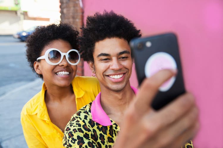 A young couple wearing yellow clothes taking a selfie in front of a pink wall