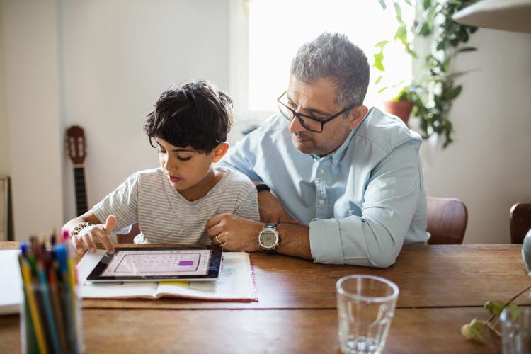 Father assisting son in using digital tablet at home