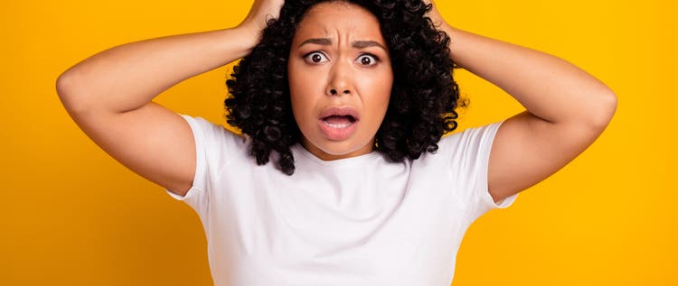 Portrait of horrified scared girl with curly hairdo wear white t-shirt holding palms on head staring isolated on yellow color background.