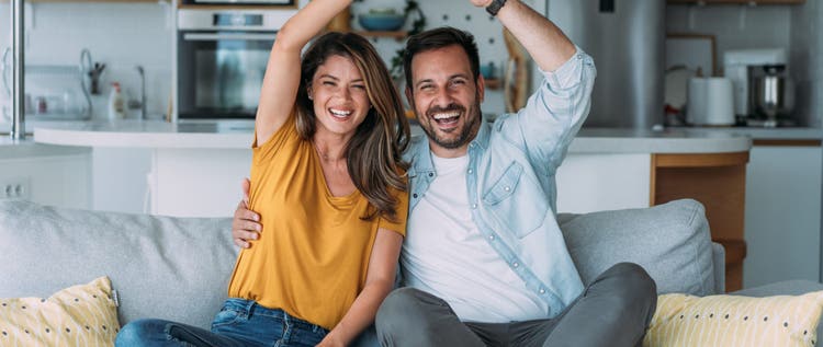 Shot of a cheerful young couple sitting on the sofa in their new home and making roof figure with hands over heads.