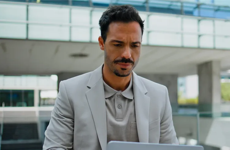 Businessman in a grey suit using a laptop outside a modern glass office building