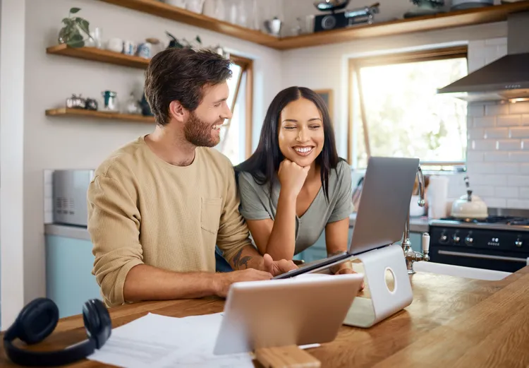 Couple smiling together as they look at a laptop in their kitchen
